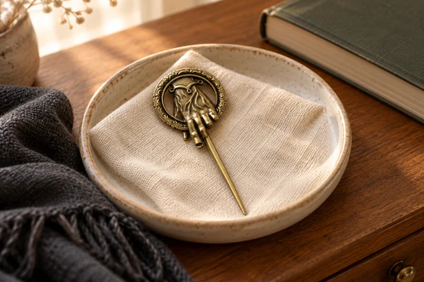 AI styling illustration of an antique gold-tone Hand of the King pin on linen in an accessory dish